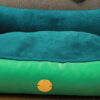 Hundebett in der Farbe türkis, grün, blau vor einer grauen Couch